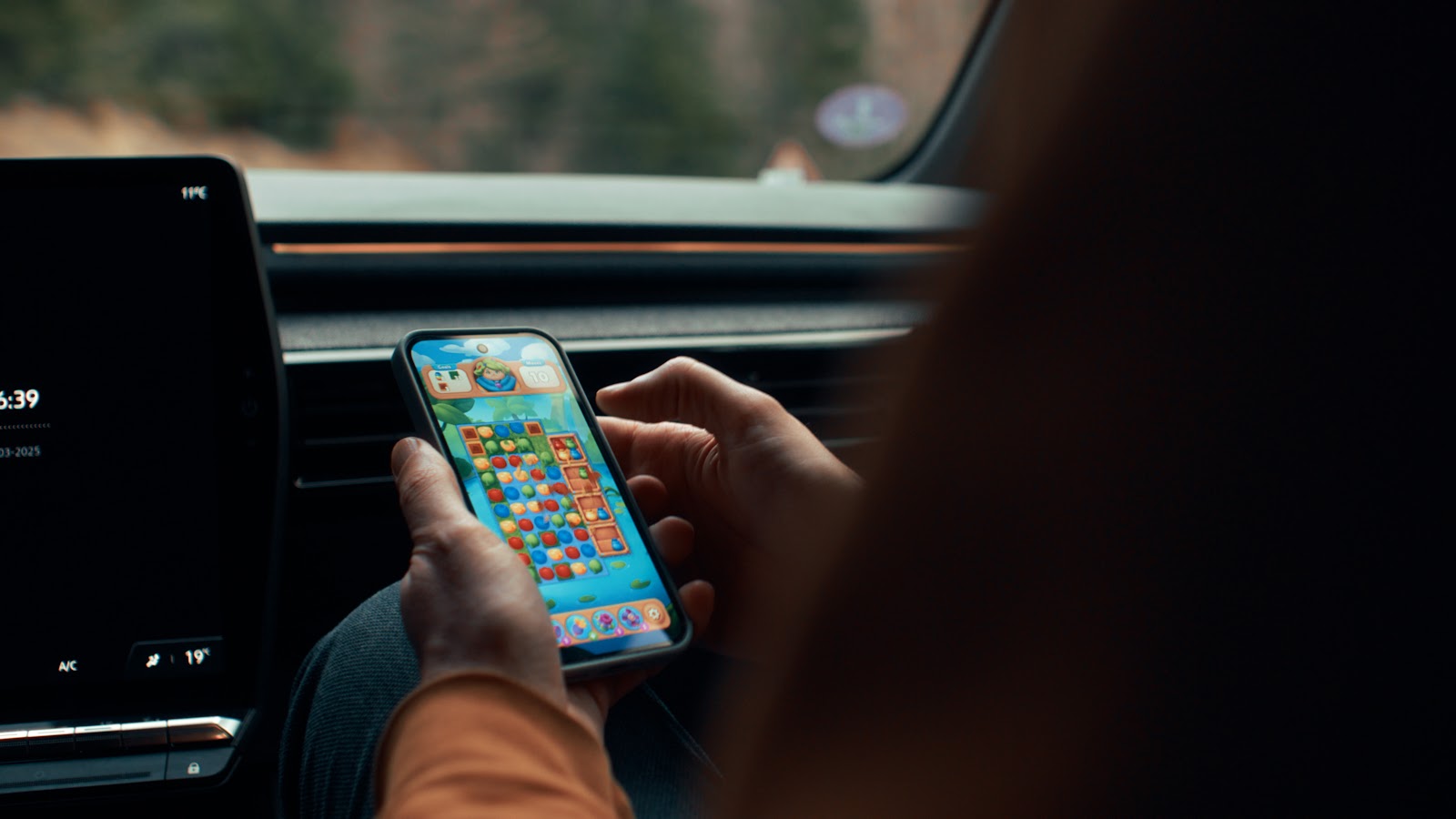 a close up of a user playing the My Lovely Planet game on their mobile device while sitting in the front seat of a vehicle